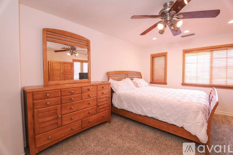 A bedroom with a large bed, a dresser with a mirror, and a ceiling fan.