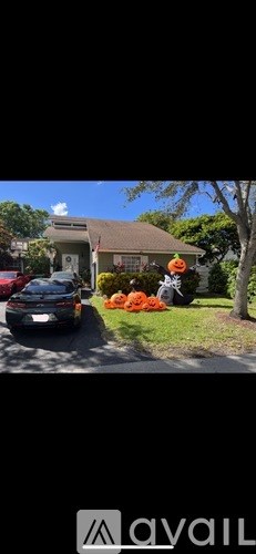 A car is parked in front of a house with a tree and pumpkins.