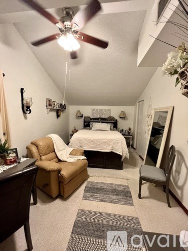 A bedroom with a bed, chair, and ceiling fan.