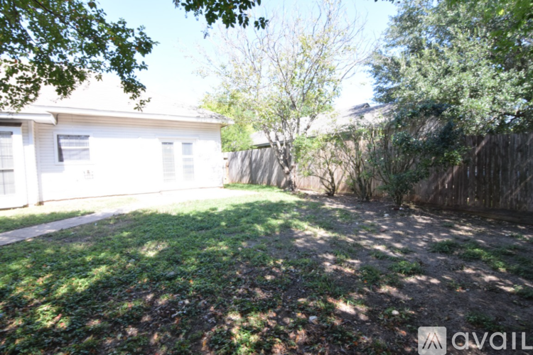 A backyard with a white house, a fence, and trees.