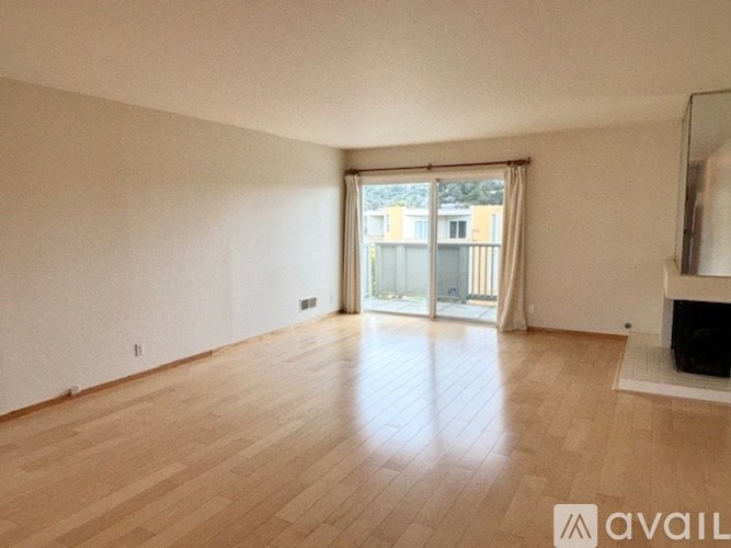 A spacious room with wooden flooring and a sliding glass door leading to a balcony.