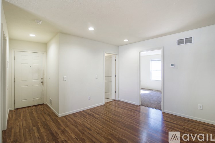 A room with wooden floors and white walls, with a door on the left and a window on the right.