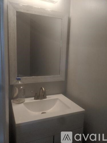 A bathroom sink under a mirror with a bottle on the counter.