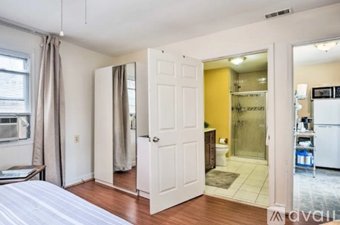 A bedroom with a bed, a white door, a window with curtains, and a kitchen area with a refrigerator and a sink.
