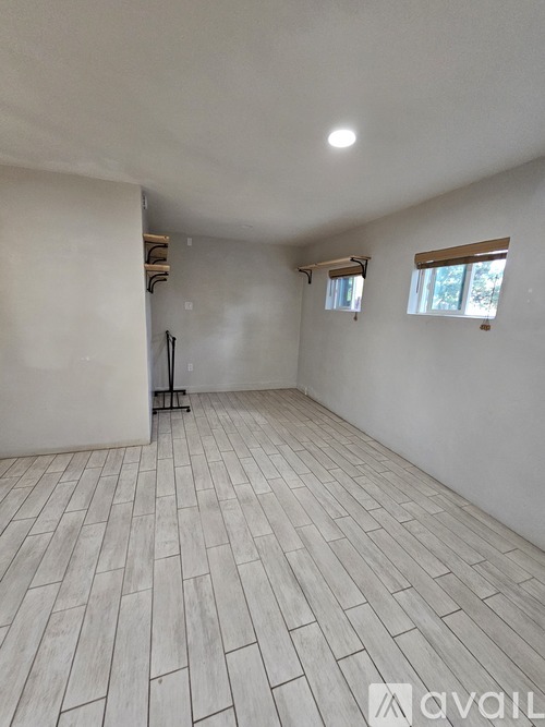 A room with wooden flooring and white walls, with a window on the right side.