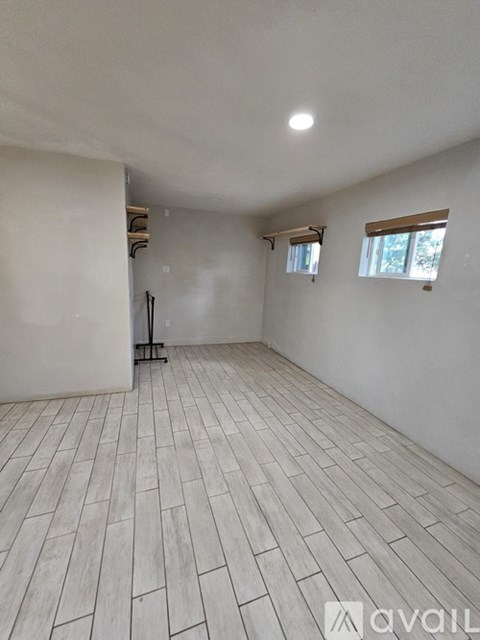 A room with wooden flooring and white walls, with a window on the right side.
