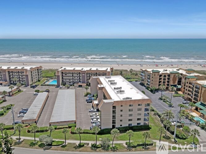 A beachfront hotel complex with a parking lot in front.
