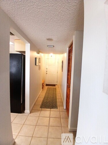 A hallway with a rug on the floor and a refrigerator on the left.
