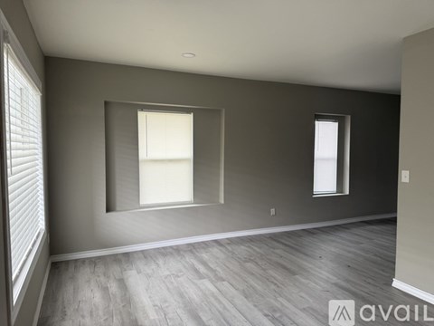 A spacious room with wooden flooring and two windows.