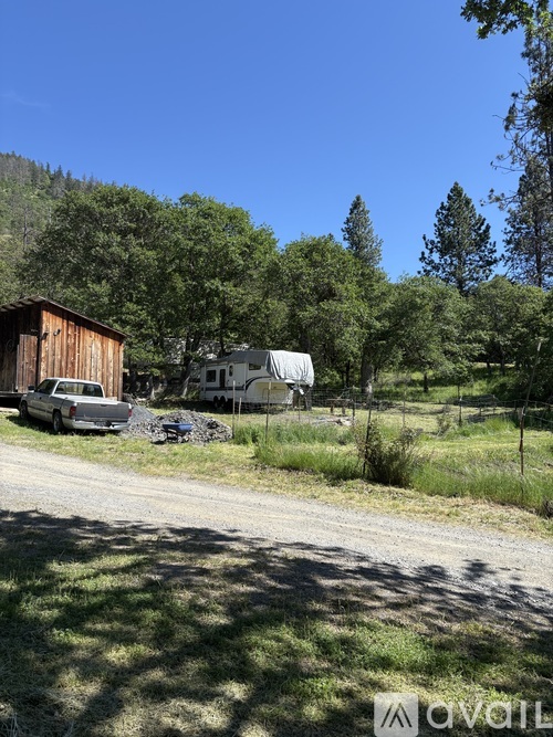 A car is parked on the side of a gravel road with trees and a mountain in the background.