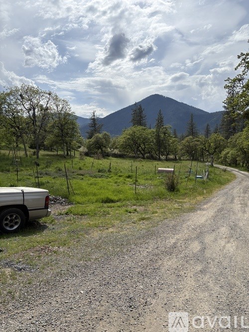 A car is parked on the side of a gravel road with trees and a mountain in the background.