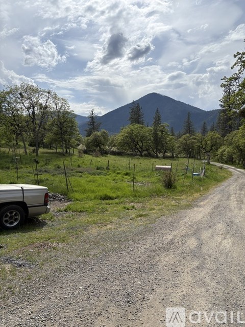 A car is parked on the side of a gravel road with trees and a mountain in the background.