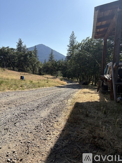 A dirt road with a wooden sign on the right side and a mountain in the background.