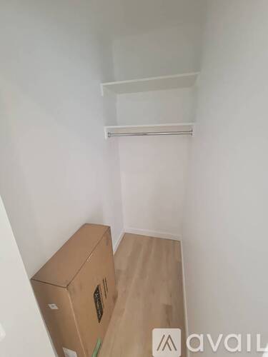A cardboard box is on the floor of a room with a shelf above it.