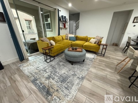 A living room with a yellow couch and a grey ottoman.