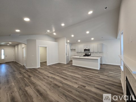 A spacious room with wooden flooring and a kitchen area with white appliances.