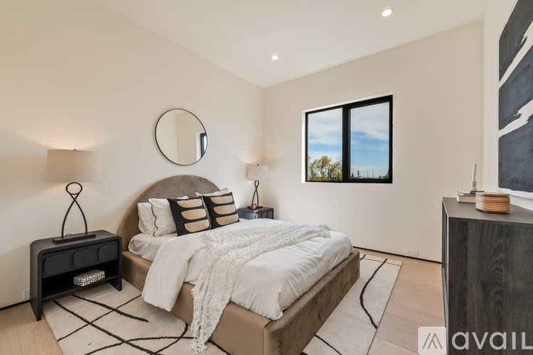 A bedroom with a large bed, a mirror, and a window with a view of trees.