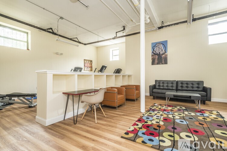 A room with a white desk, a black couch, and a rug with multicolored circles.