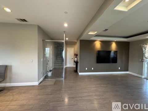 A spacious living room with a television and a staircase in the background.