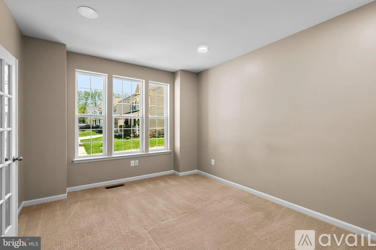 A room with beige walls and carpet, with a window showing a view of a house and trees.