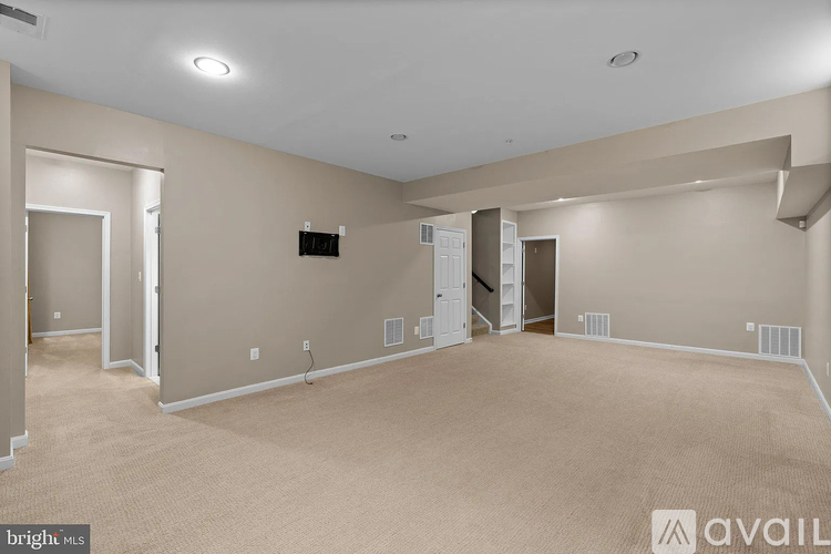 A spacious room with beige carpeting and white walls, with a flat-screen TV mounted on the wall.