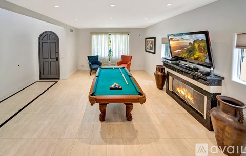 A pool table with a green cloth and a television on a stand with a fireplace in the background.
