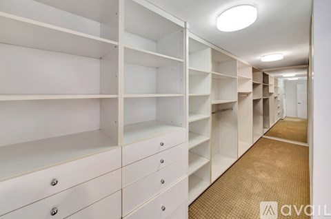 A long hallway with white shelves and drawers on the side.