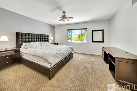 A bedroom with a large bed, a desk, and a ceiling fan.