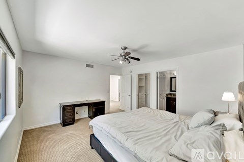 A bedroom with a bed, desk, and ceiling fan.
