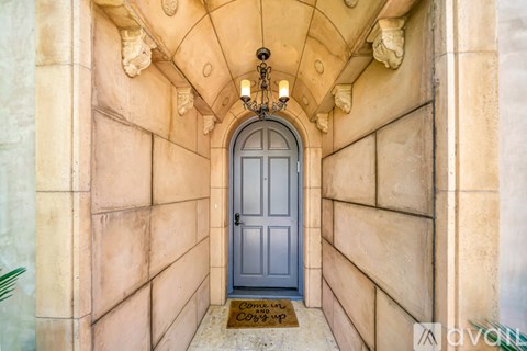 A grey door is at the end of a hallway with a chandelier hanging from the ceiling.