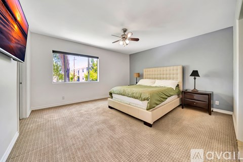 A bedroom with a large bed, a ceiling fan, and a window with a view of the outside.