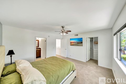 A bedroom with a bed, a ceiling fan, and a window with a view of the outdoors.