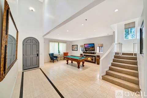 A spacious living room with a pool table and a staircase.