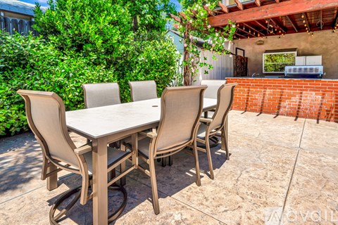 A patio with a table and chairs is surrounded by greenery.