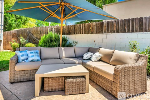 A patio with a sofa, table and umbrella.