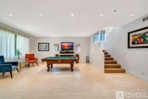 A spacious living room with a pool table and a staircase.