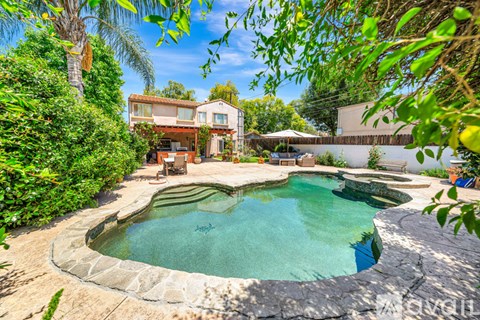 A pool surrounded by greenery and a house in the background.