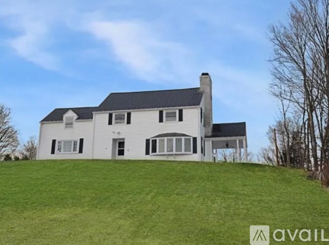 A large white house with a black roof is situated on a grassy hill.