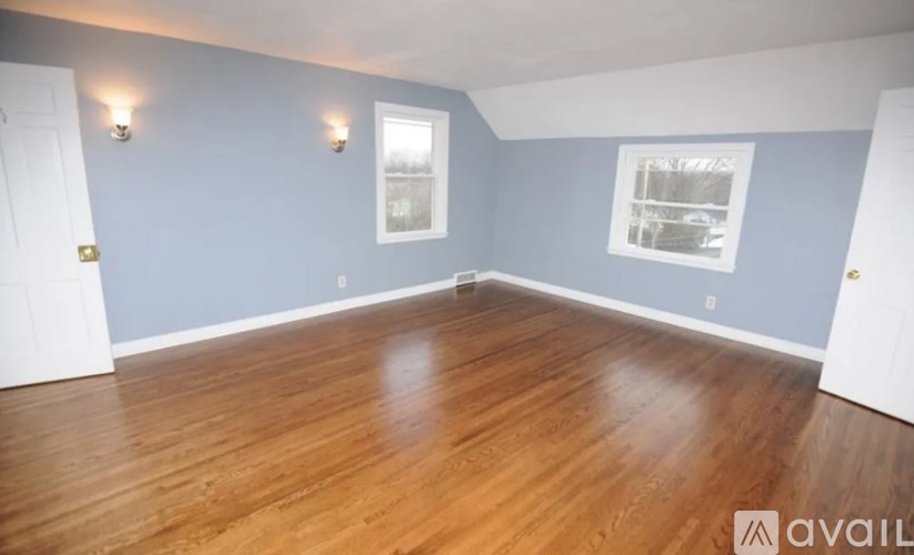 A room with wooden flooring and two windows.
