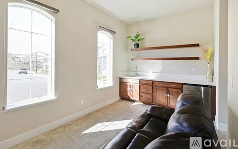 A living room with a black leather couch and a window overlooking a street.