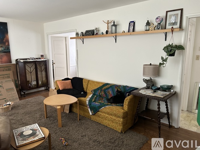 A living room with a yellow couch, a wooden table, and a shelf with various decorations.