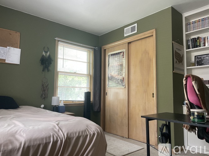 A bedroom with a bed, a window, a door, and a table with a red object on it.