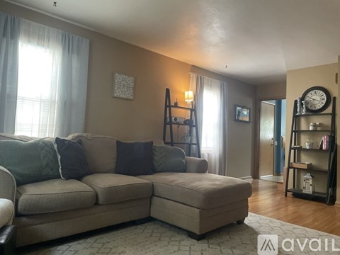 A living room with a beige couch and a clock on the wall.