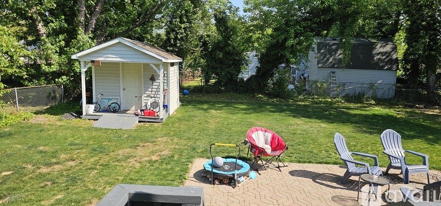 A small white shed sits in a grassy backyard with a table and chairs.