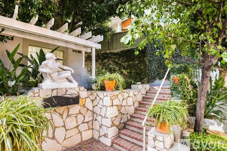 A white statue of a woman sits on a stone wall in front of a house.