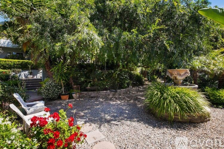 A garden with a bench, a fountain, and red flowers.
