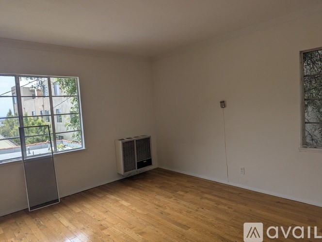 A room with wooden flooring and a window overlooking a tree-filled street.