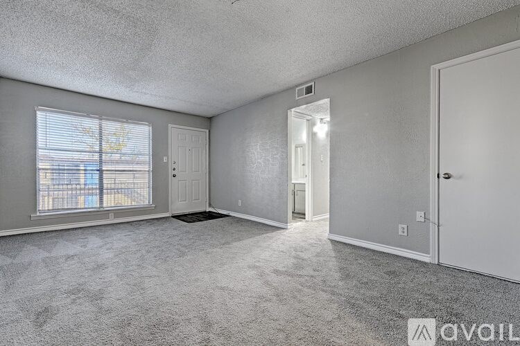 A sparsely furnished room with a carpeted floor and a window with blinds.