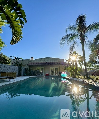 A pool with a house and palm trees in the background.
