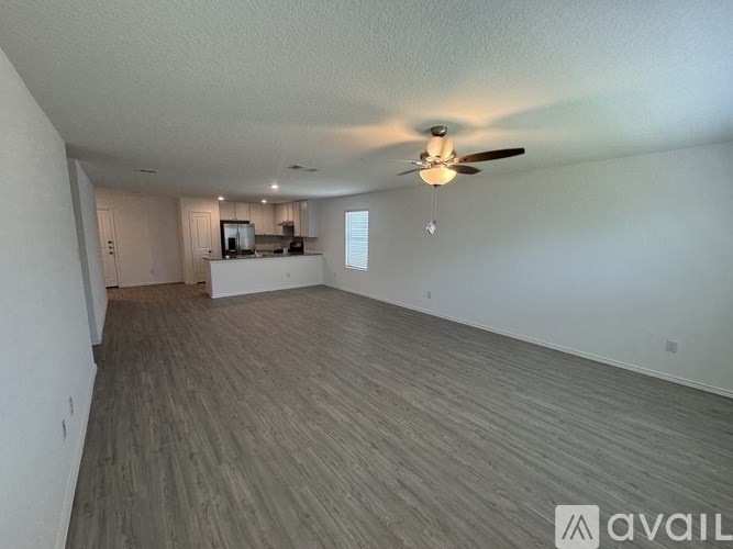 A spacious living room with a ceiling fan and a kitchenette in the background.